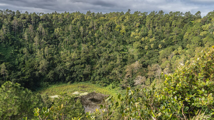 The crater of an extinct volcano. At the bottom you can see a lake surrounded by thickets of lush green rainforest. Blue sky, clouds. Mauritius. Trou-aux-Cerfs. Murr's Volcano