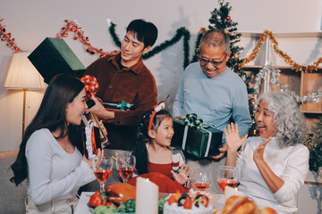 Portrait of Asian family exchanging presents during christmas at home. Attractive happy people holding gift box, celebrate holiday thanksgiving, xmas eve tradition in living room in house together.