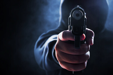 Closeup of hooded man hand holding a gun on dark smoke background