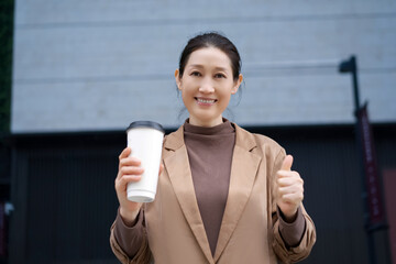 Happy Woman Enjoying Coffee While Giving Thumbs Up Outdoors