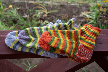 Striped socks knitted from orange, yellow, gray and green yarn lie on the terrace railing