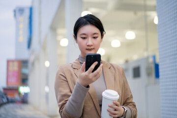 Young Woman Engaged with Smartphone While Holding Coffee in Urban Setting