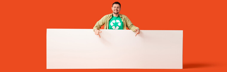 Young man wearing t-shirt with recycling sign pointing at blank poster on orange background....