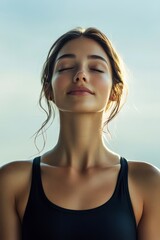 Fototapeta premium A serene young woman with closed eyes, breathing deeply, radiates tranquility against a soft, cloudy background.