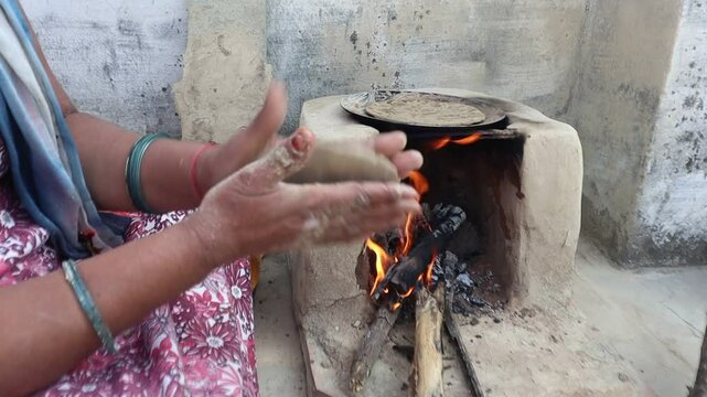 Indian woman cooking bajre ki roti on a traditional clay chulha, showcasing rural lifestyle and traditional cooking methods.