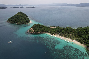 Fototapeta premium Aerial picture of a remote island next to Port Barton in the Philippines. Holidays in Asia, hopping island activity. Beautiful bay, white beach, coconut trees, coral reef and blue ocean with boats.