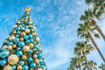 Festive Christmas tree adorned with blue and gold ornaments against a vibrant blue sky and palm trees. AI.