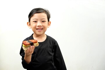 A cheerful boy in a black shirt smiles while holding a delicious spam musubi. The minimalistic...