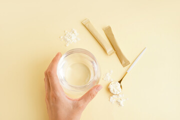 Female hand with glass of water, collagen powder and spoon on yellow background