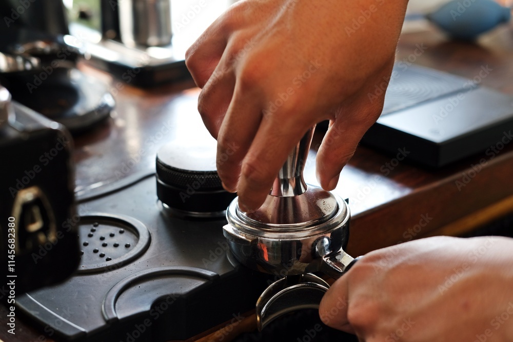 Wall mural Close-up barista hands pressing espresso grounds with a tamper on a coffee machine portafilter, preparing for a fresh espresso shot. Ideal for barista, coffee culture, and artisanal coffee content.