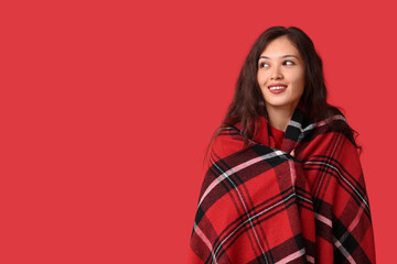 Fototapeta premium Beautiful young happy Asian woman with checkered soft plaid on red background