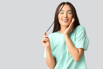 Happy young Asian woman with stylish mint makeup on grey background