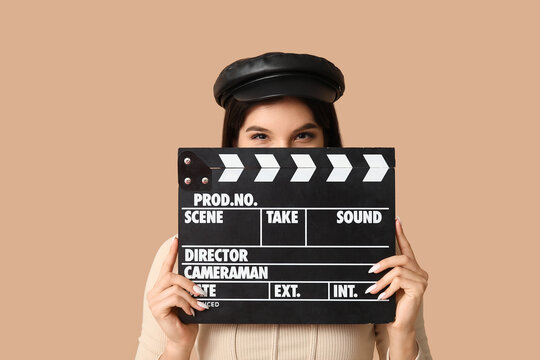 Young woman in beret holding film clapperboard over face, movie production and filmmaking industry