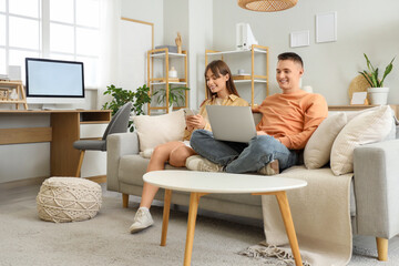 Young couple using laptop and mobile phone on sofa at home