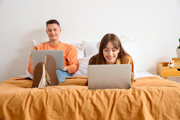 Young couple using laptops in bedroom