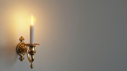 An elegant gold candle sconce with a lit candle, casting warm light on a smooth white wall.