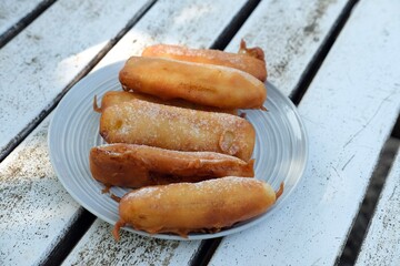 Close-up of golden crispy pisang goreng or banana fritters dusted with powdered sugar,served on a...