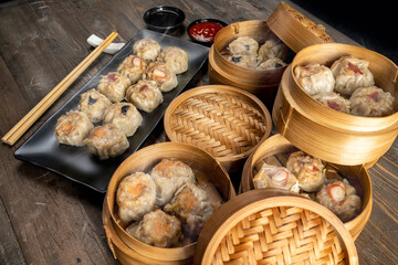Assorted chinese dim sum dumpling on the plate with bamboo wooden basket bowl and chopstick with sauce on wooden table