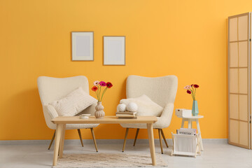 Armchairs and gerbera flowers on coffee table in living room