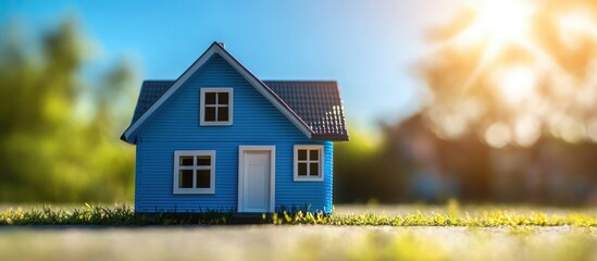 Miniature blue toy house on green grass with lens flare under a bright blue sky creating a cheerful and inviting atmosphere