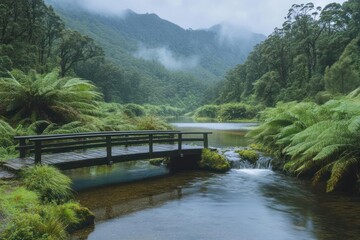 Fototapeta premium A serene river scene with a wooden bridge surrounded by lush greenery and misty mountains.
