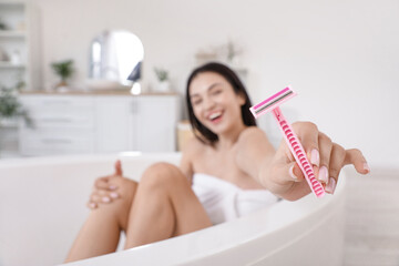 Obraz premium Beautiful young happy woman with razor sitting in bathtub at home