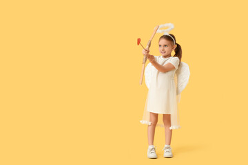 Cute little girl dressed as Cupid with arrow and bow on yellow background. Valentine's Day celebration