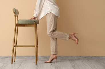 Elegant woman in heels and stool near beige wall