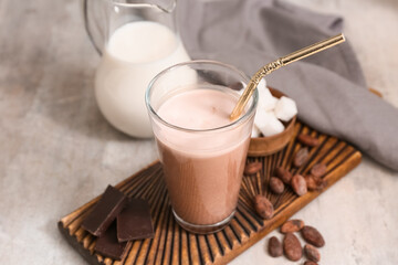 Glass of sweet chocolate milk with cocoa beans and cubes of sugar on grey background