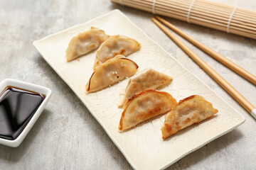 Plate with fried Japanese gyoza and bowl of soy sauce on grey background, closeup