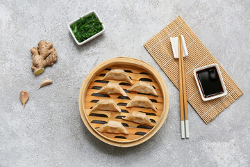 Bamboo steamer with tasty Japanese gyoza and bowls of soy sauce and seaweed salad on grey background
