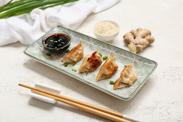 Plate of fried Japanese gyoza with green onion, sesame seeds and bowl of soy sauce on white background