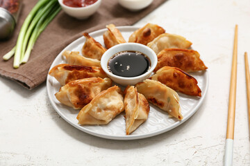 Plate of fried Japanese gyoza with bowl of soy sauce and green onion on white background, closeup