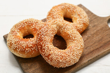 Cutting board of tasty bagels with sesame seeds on white wooden background