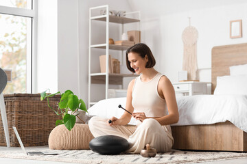 Meditating young woman playing glucophone on carpet in bedroom