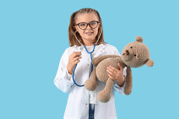Cute doctor with stethoscope and toy bear on blue background