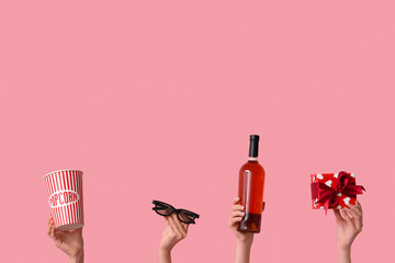Female hands with bucket of popcorn, bottle of wine, gift box and 3D glasses on pink background....