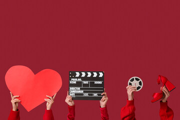 Female hands with paper heart, film reel, movie clapper and heeled shoe on red background....