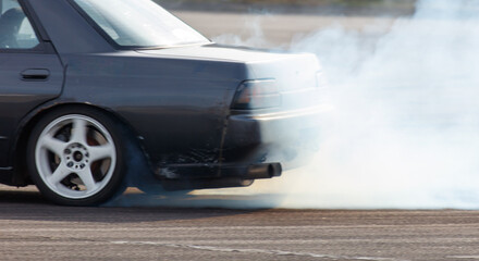 A black car is driving down a road with smoke coming out of its tailpipe