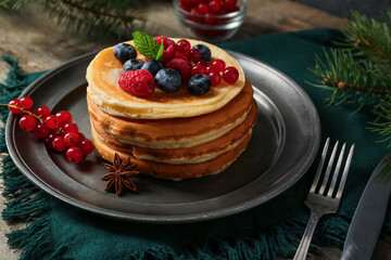 Plate of sweet pancakes with berries and Christmas tree branch on wooden background