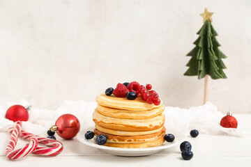 Plate of sweet pancakes with berries, candy canes, Christmas tree and balls on white wooden table