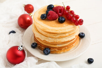 Plate of sweet pancakes with berries and Christmas balls on white wooden background