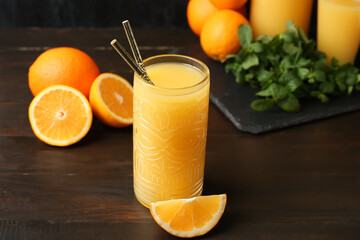 Glass of tasty juice with straws and orange slice on wooden table