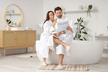 Loving couple reading newspaper after shower in bathroom
