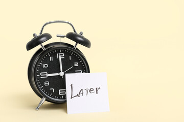 Paper sheet with word LATER and alarm clock on color background