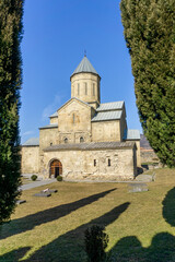 Tsilkani Cathedral Church. Stone walls, dome with a cross. Courtyard with green grass, tall cypresses with shade.