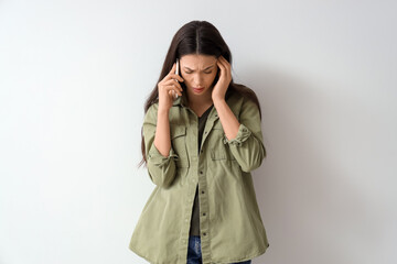 Portrait of worried young woman talking by mobile phone on light background
