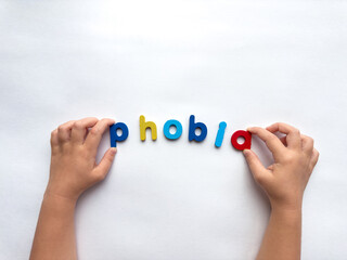 Childs hands spelling phobia with colorful letters on white background