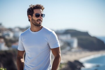 A man wearing a white shirt and sunglasses is standing on a beach
