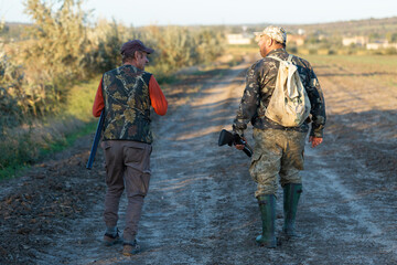 Mature hunter man holding a shotgun and walking through a field
